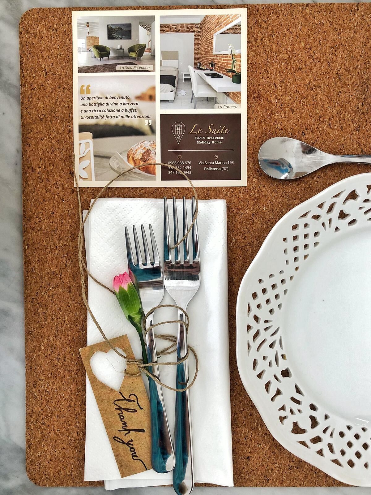 A cork placemat with a brochure, a set of cutlery, a napkin, a glass, and a plate.