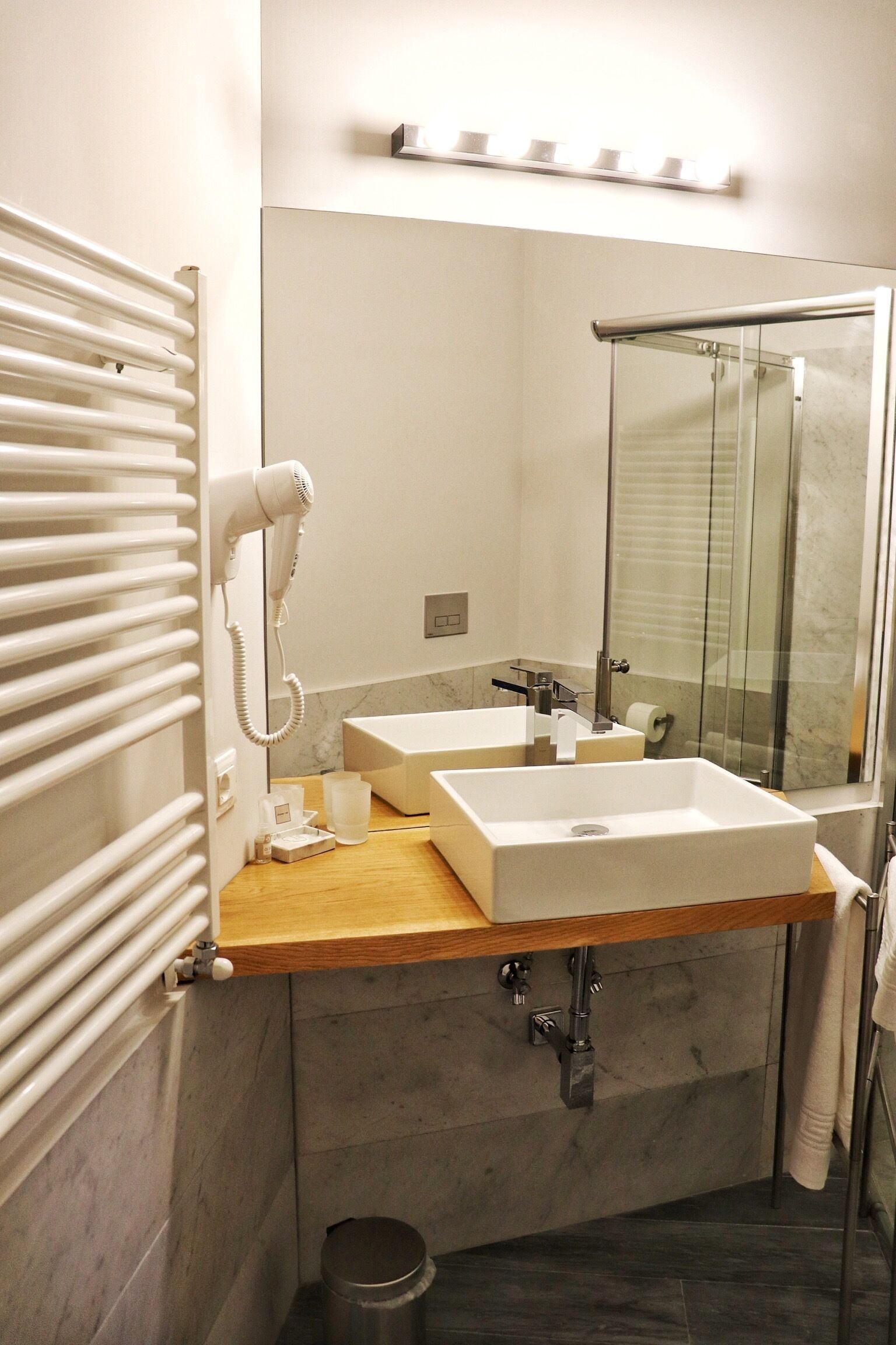 Un baño moderno con un espejo grande, dos lavamanos, un secador de pelo y una ducha.