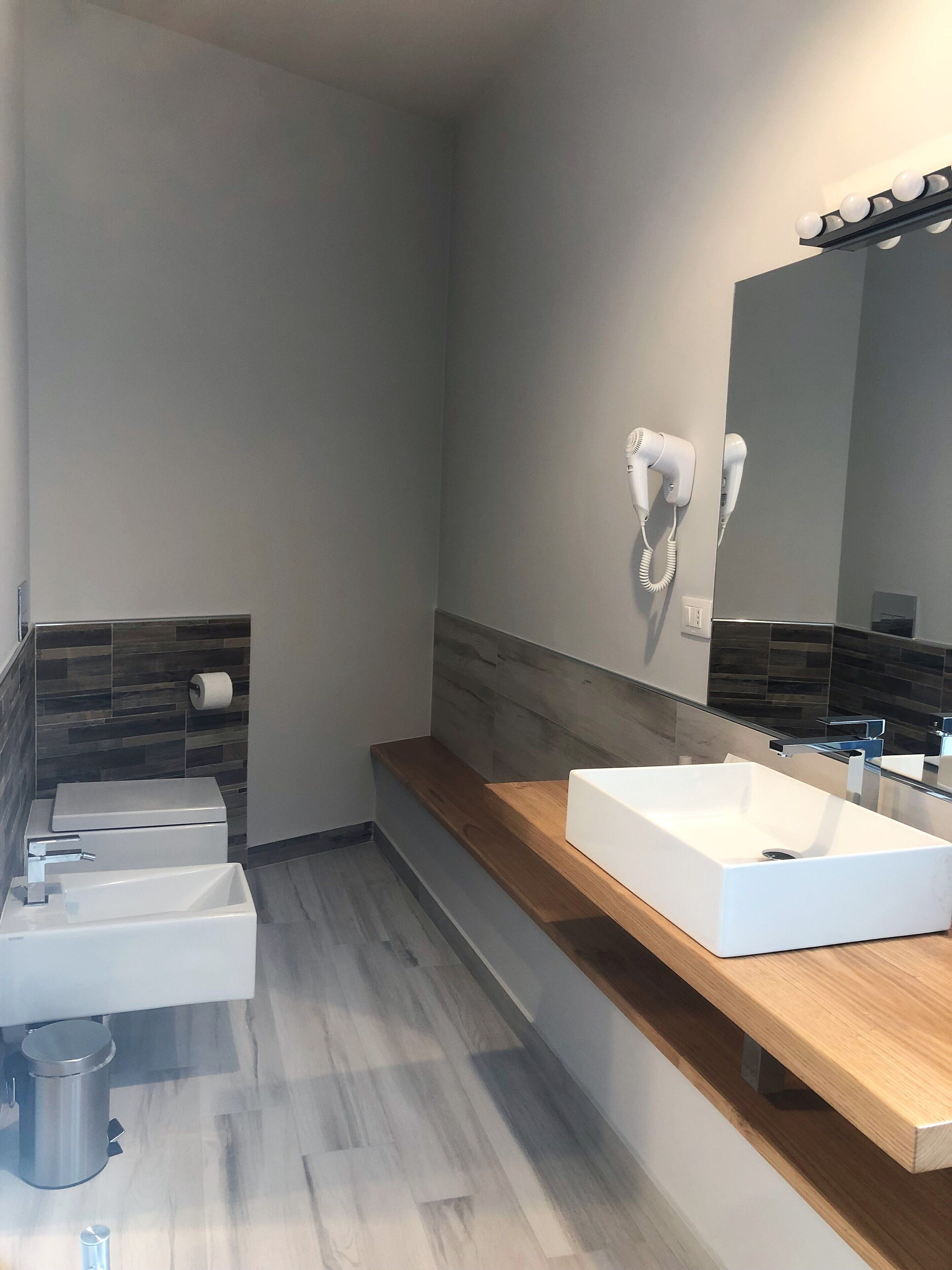 A modern bathroom with a white sink, a mirror, and a hairdryer mounted on the wall.