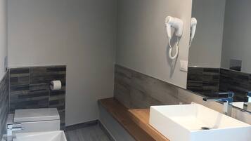 A modern bathroom with a white sink, a mirror, and a hairdryer mounted on the wall.