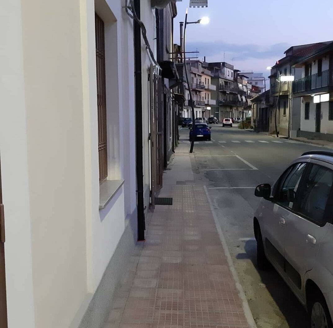 Une rue étroite bordée d’immeubles, une voiture garée et un trottoir pour les piétons.