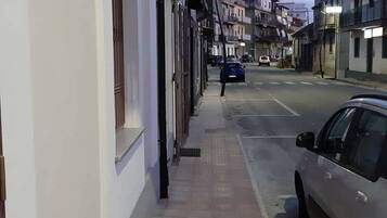 Une rue étroite bordée d’immeubles, une voiture garée et un trottoir pour les piétons.