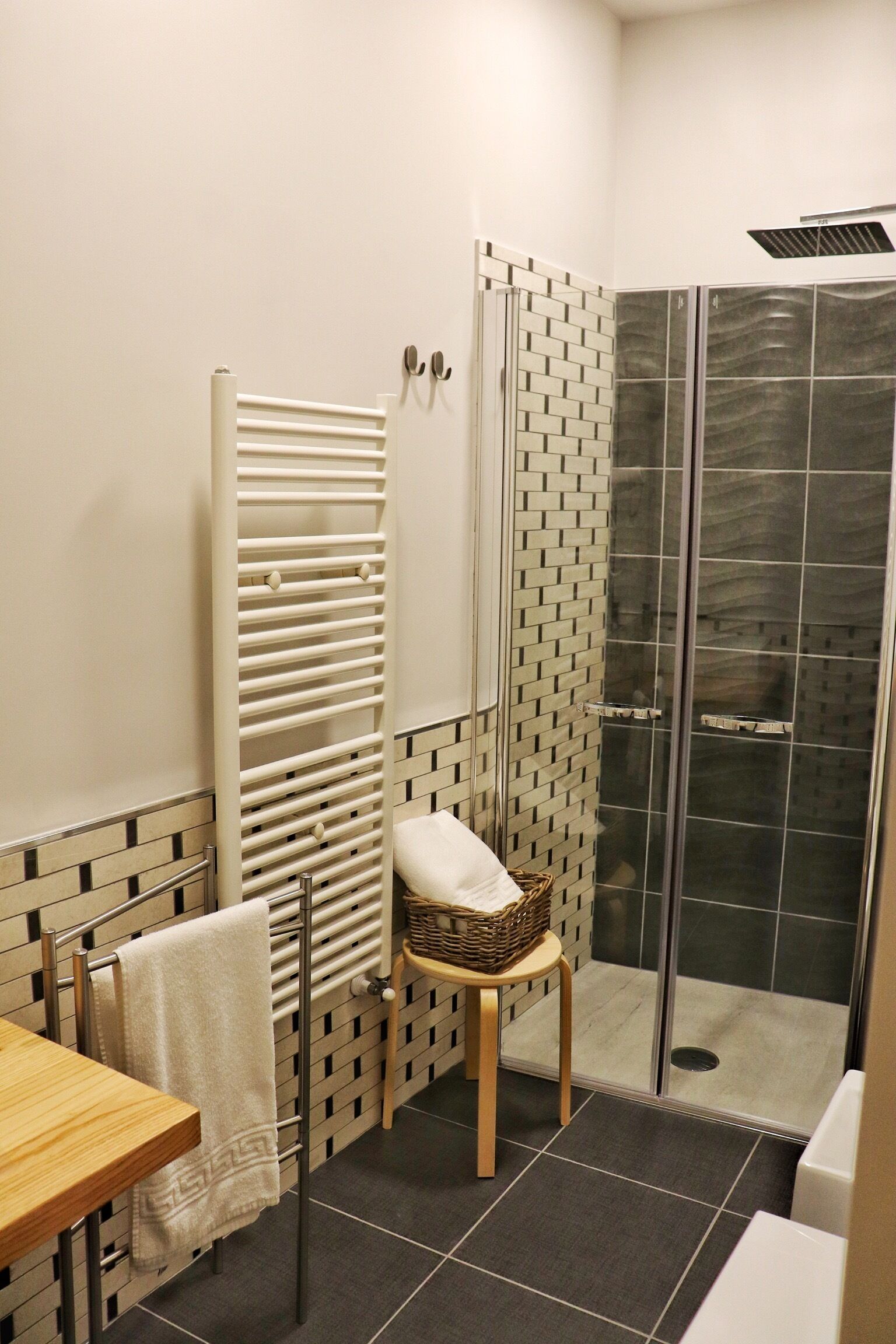 Un baño con ducha, un perchero, una cesta de mimbre y un taburete de madera.