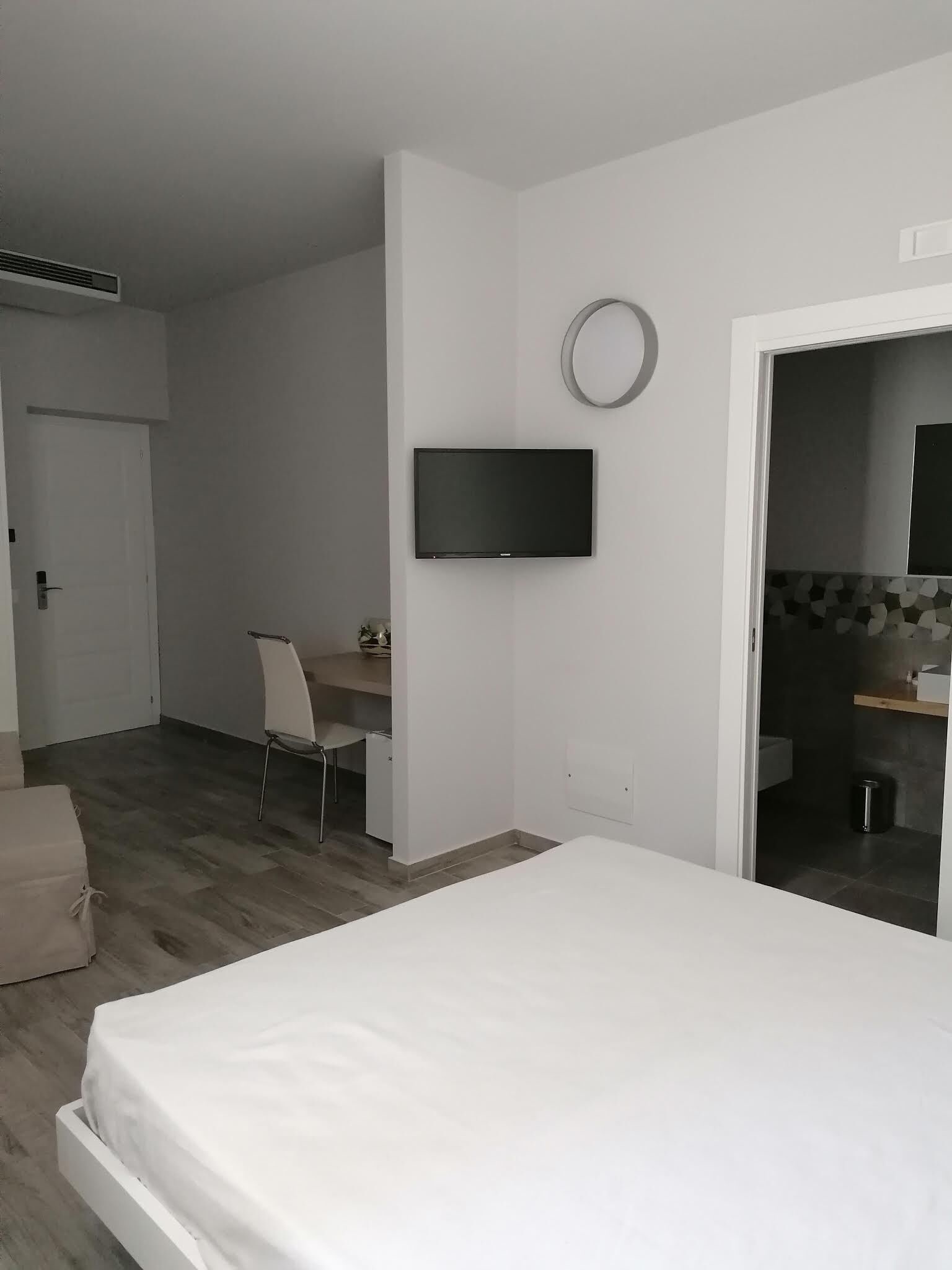 Un dormitorio con cama, escritorio, silla, televisor y baño visible a través de una puerta abierta.