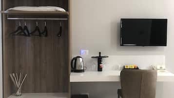 Une chambre moderne équipée d’une armoire en bois, d’un bureau blanc, d’un téléviseur à écran plat, d’une bouilloire, d’un porte-verres à vin et d’une chaise.