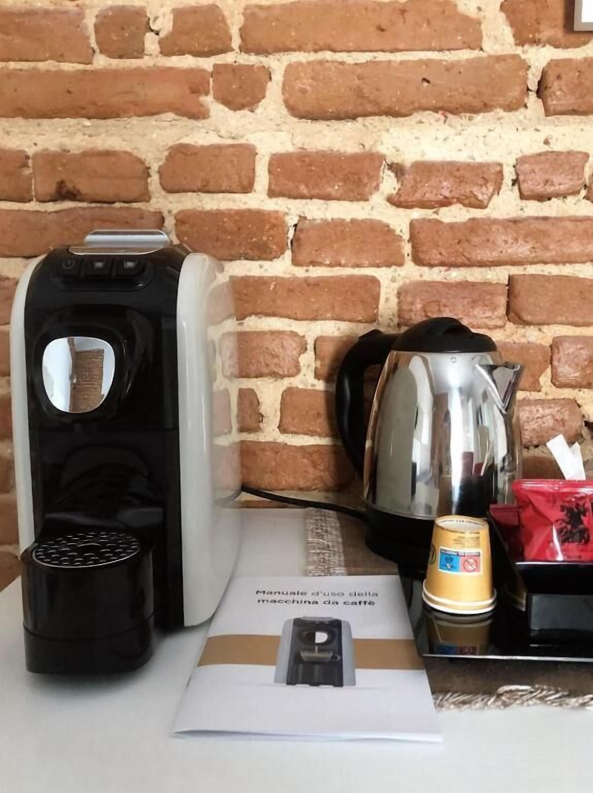 A coffee maker, a kettle, and a manual on a table against a brick wall.