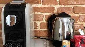 A coffee maker, a kettle, and a manual on a table against a brick wall.