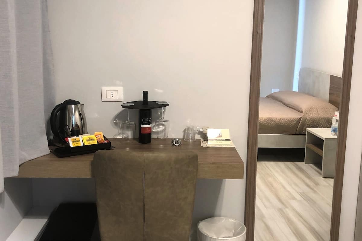 Habitación de hotel con escritorio, silla, cafetera, botella de vino y cama con cabecera.