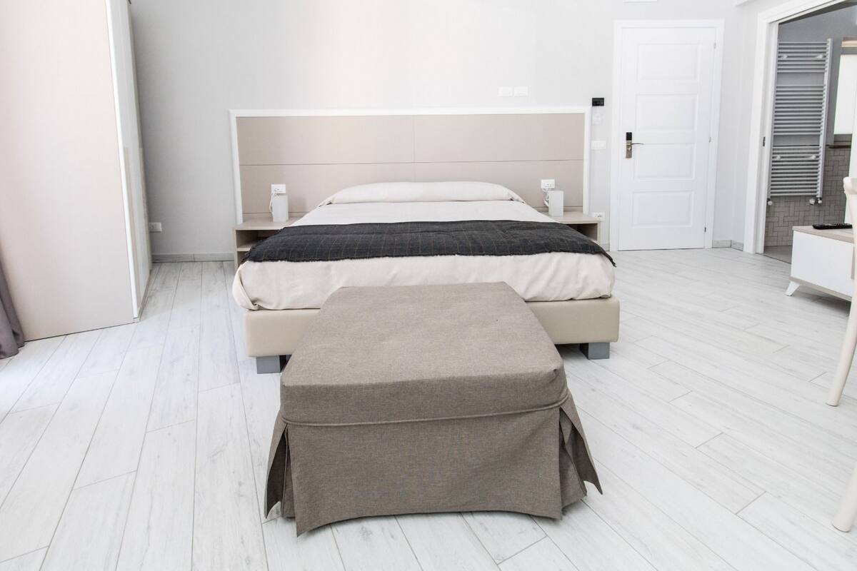 Una habitación de hotel moderna con una cama, mesitas de noche, un banco y un armario.