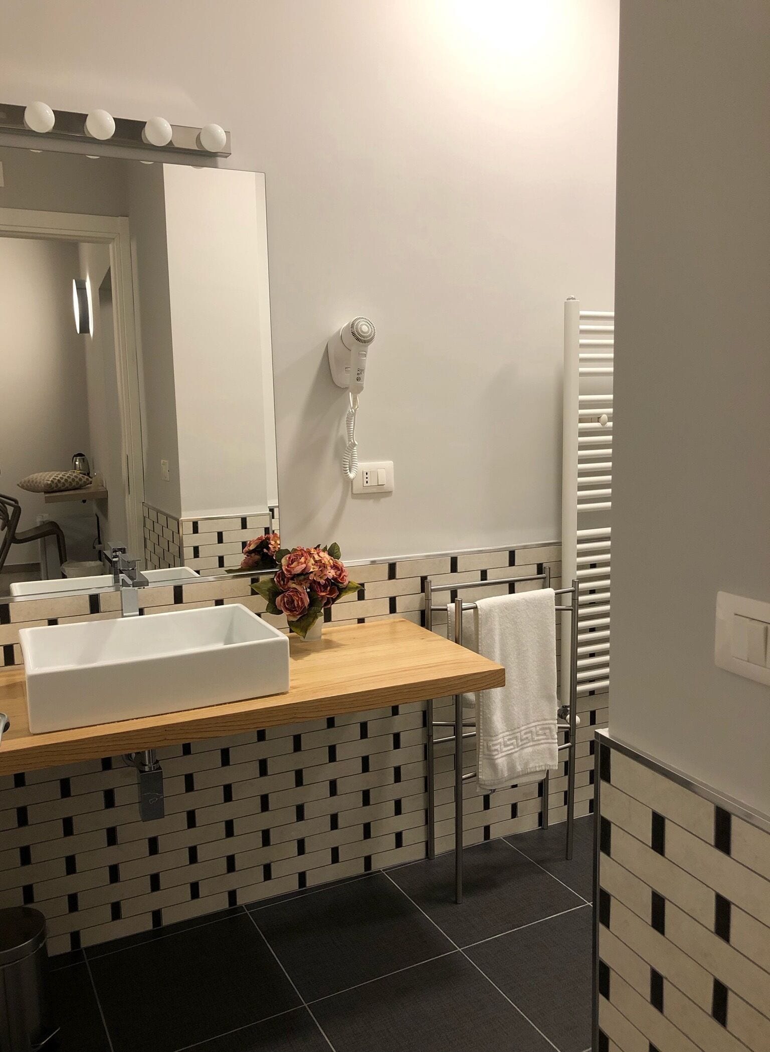 A modern bathroom with a rectangular sink, a mirror, a hairdryer, and a towel rack.