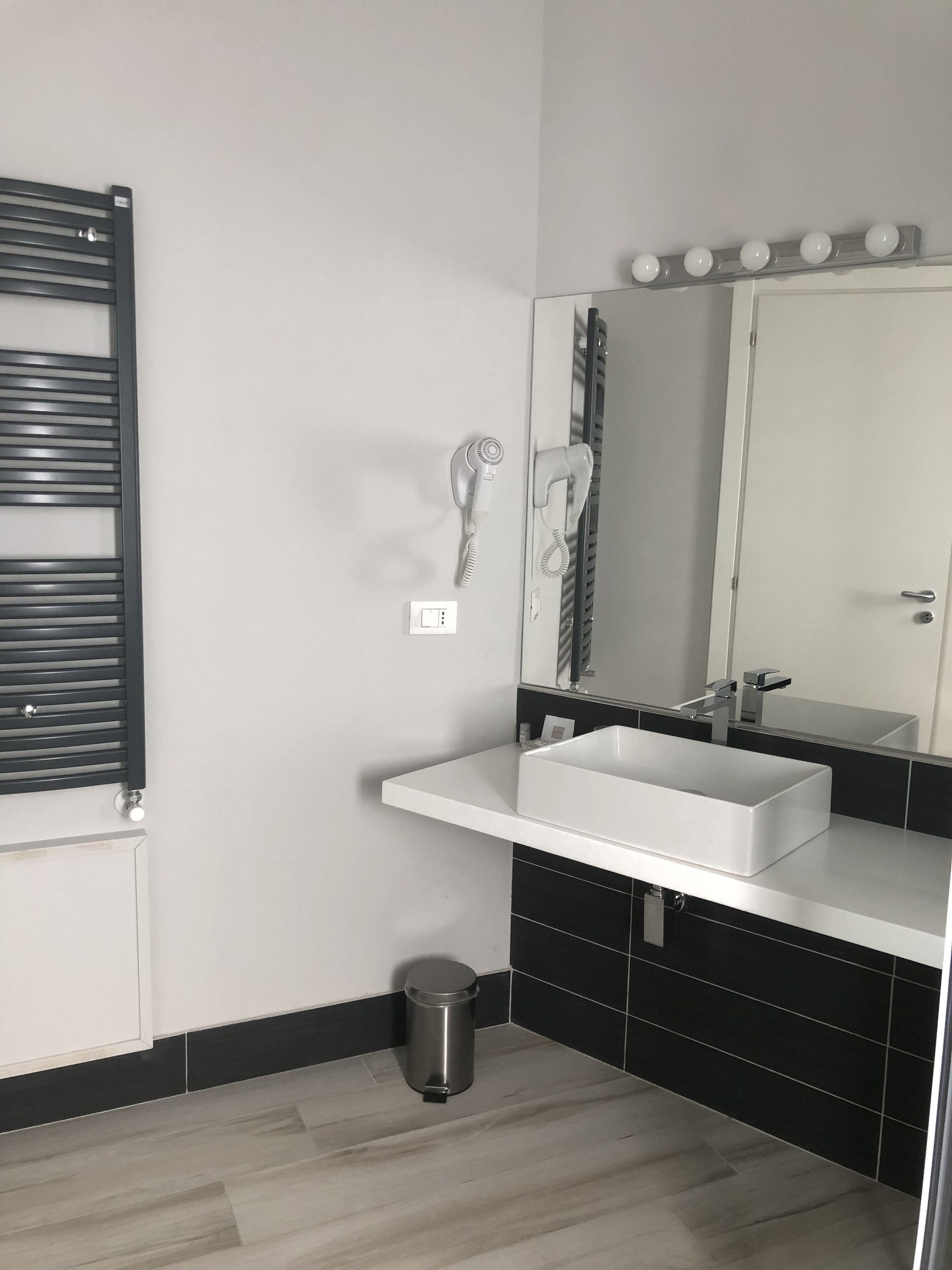 A modern bathroom with a white sink, black and white tiles, a mirror with lights, and a hairdryer.