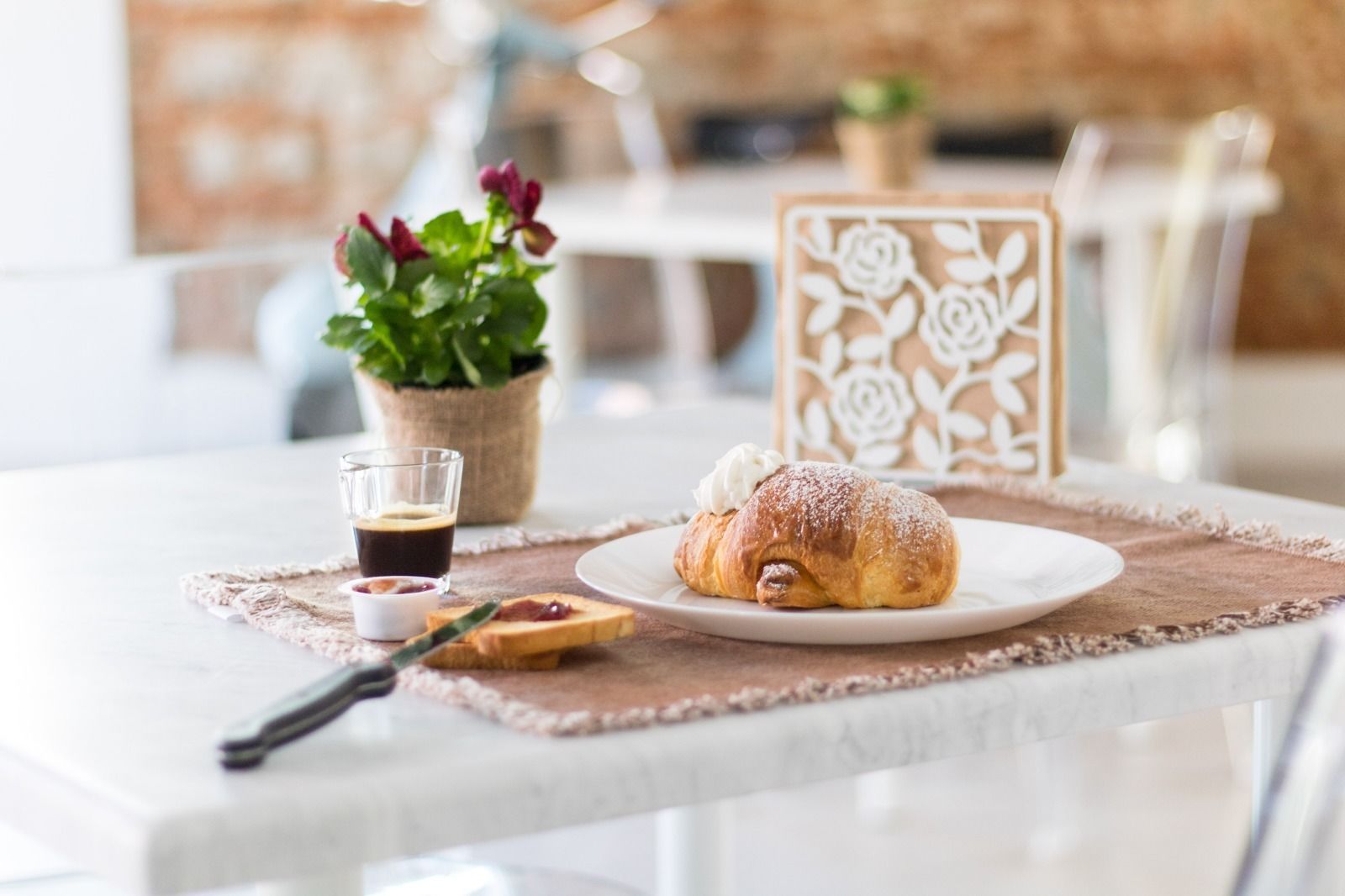 Un croissant su un piatto con zucchero a velo, una tazzina di caffè e un coltello su un sottopiatti.