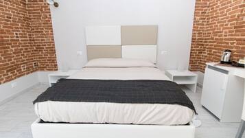A modern bedroom with a brick wall, a white bed, a bedside table, and a small white cabinet.