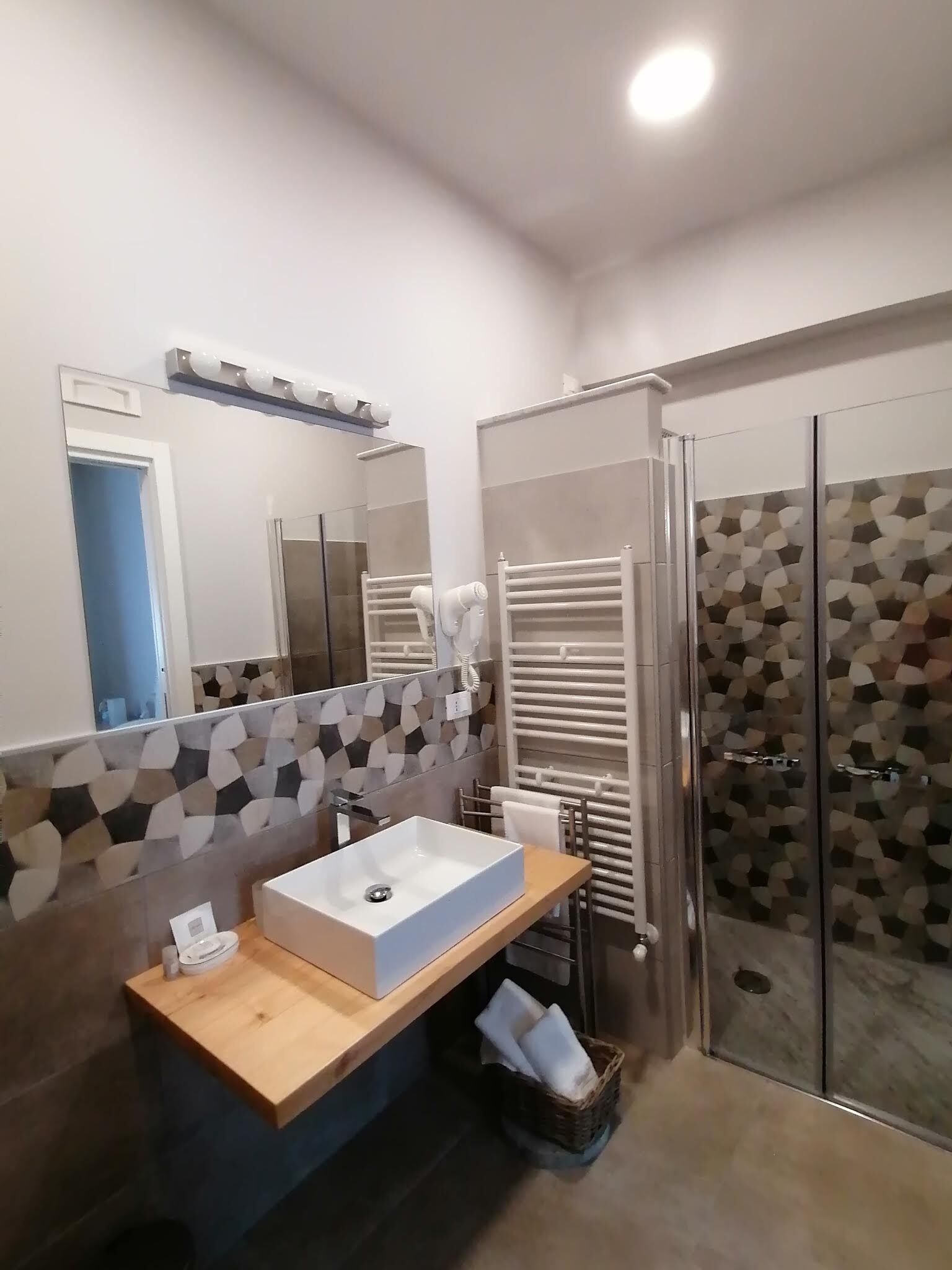 Un bagno moderno con un grande specchio, un lavandino bianco, un porta asciugamani e una doccia.