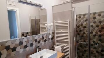 Un bagno moderno con un grande specchio, un lavandino bianco, un porta asciugamani e una doccia.