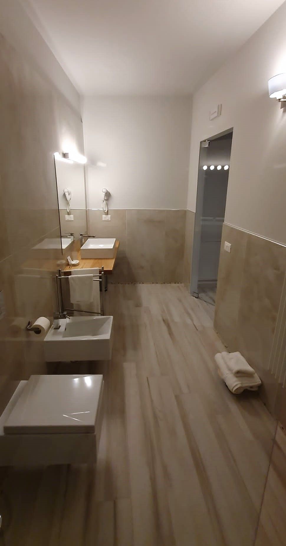 Un baño con espejo, dos lavamanos, toallero y retrete.