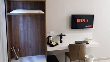 Una stanza con un'unità a scaffali in legno, una scrivania con una sedia, un televisore che mostra 'NETFLIX' e una macchina per il caffè.