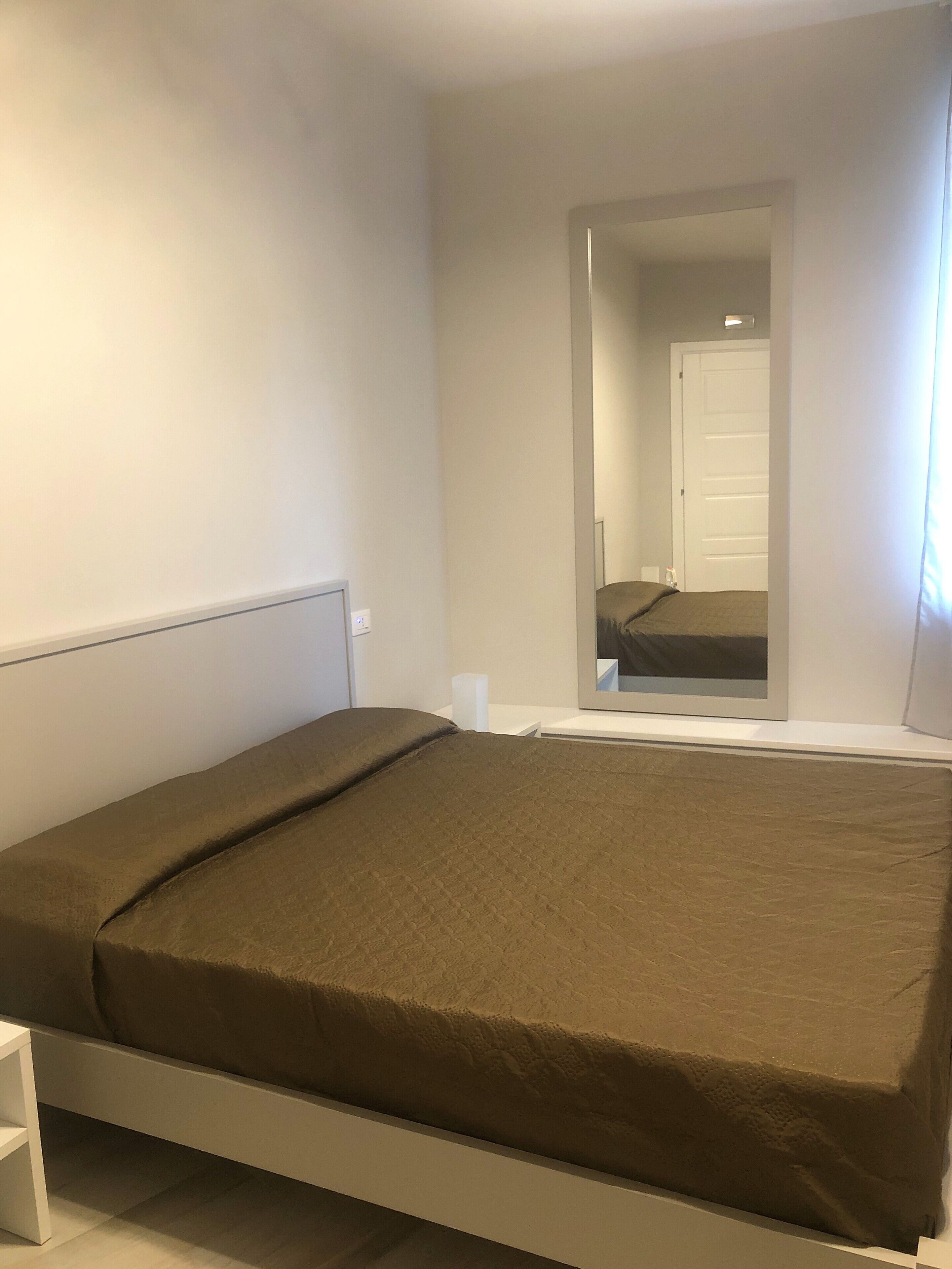 Un dormitorio con cama, mesita de noche, espejo y puerta.
