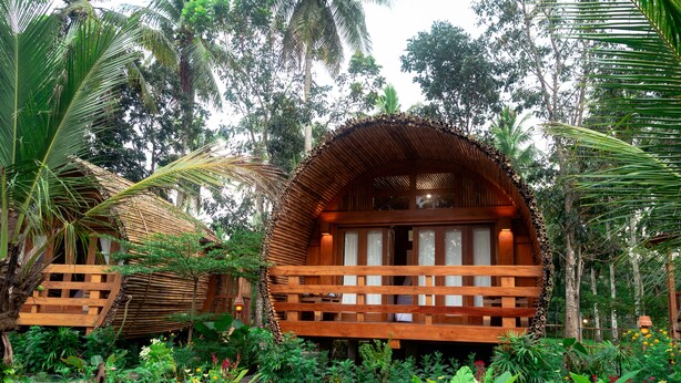 A wooden structure with a thatched roof surrounded by lush greenery and tropical plants. - Lagoona Beach Bungalows (Cijulang)
