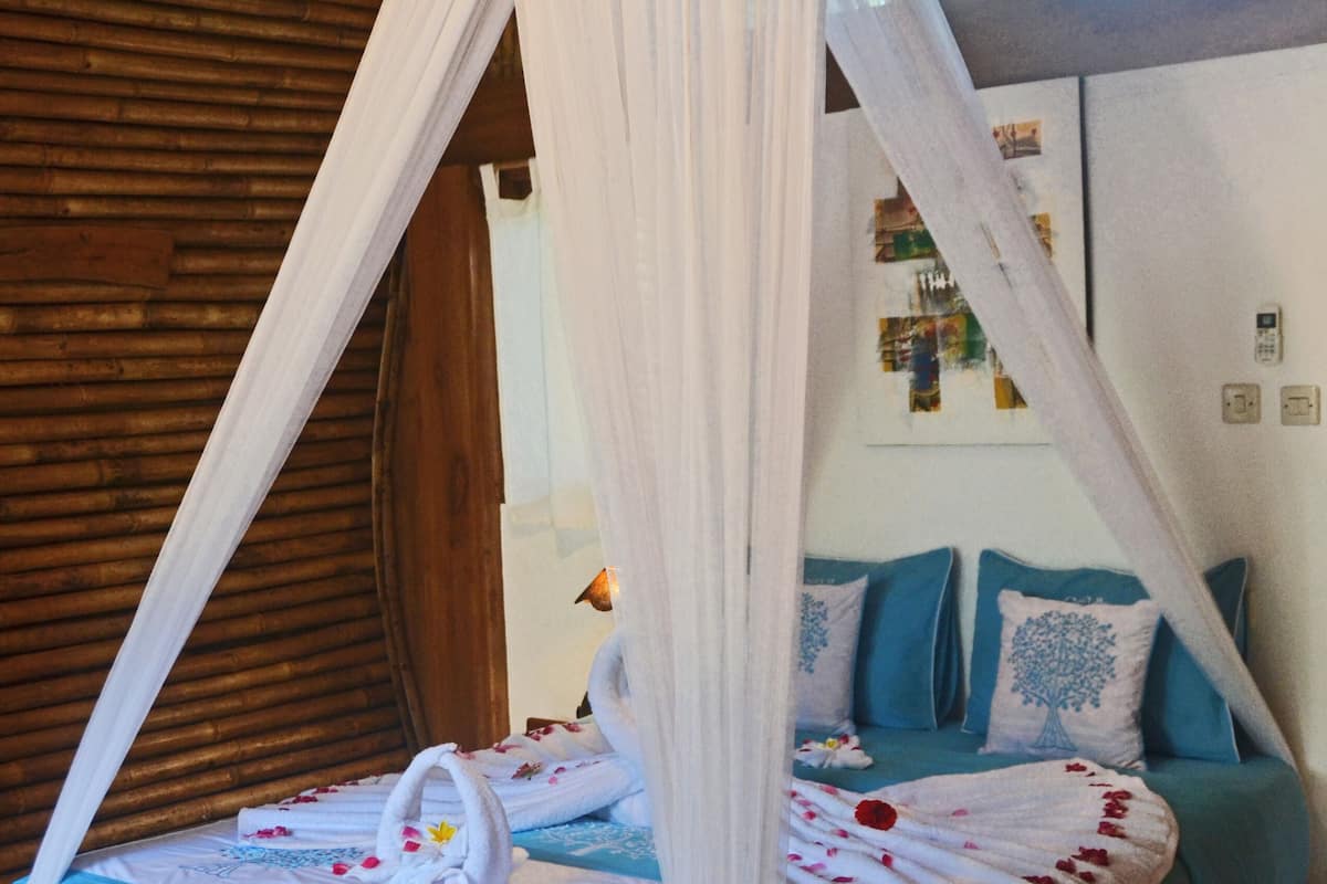 Een bed met hemelbed, houten wanden en een blauw beddekleed.