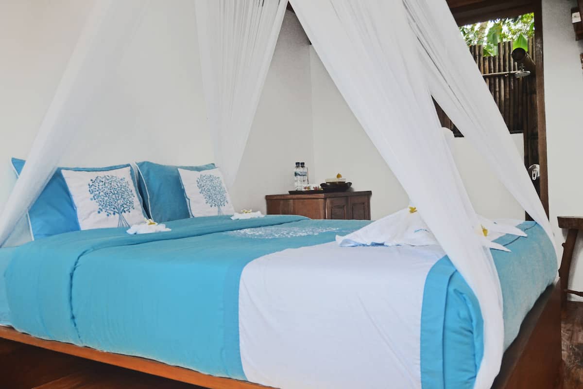 Een bed met hemelbed, blauw beddengoed en een nachtkastje met een waterfles en een kom.