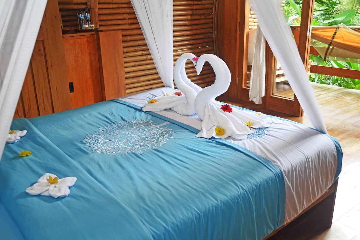 Een bed met een blauwe sprei, een witte hemel en handdoeken in de vorm van zwanen.