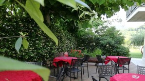 Un'area patio all'aperto con tavoli e sedie coperte da tovaglie rosse, immersa nel verde e con pavimento in pietra.