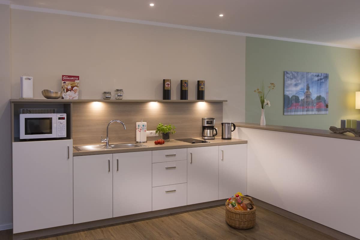 A modern kitchen with a microwave, coffee maker, and sink. There are cabinets, a basket, and a small plant on the counter.