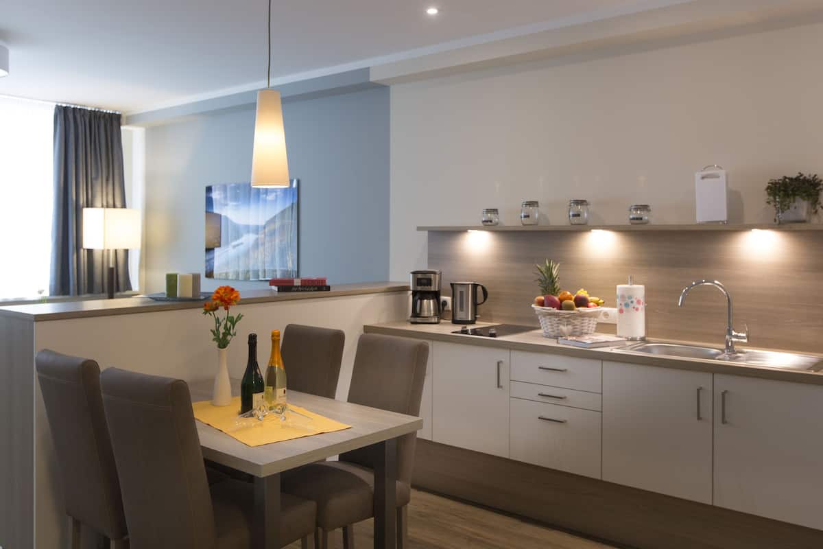 A modern kitchen with a dining area, featuring a coffee maker, fruit bowl, and a sink.