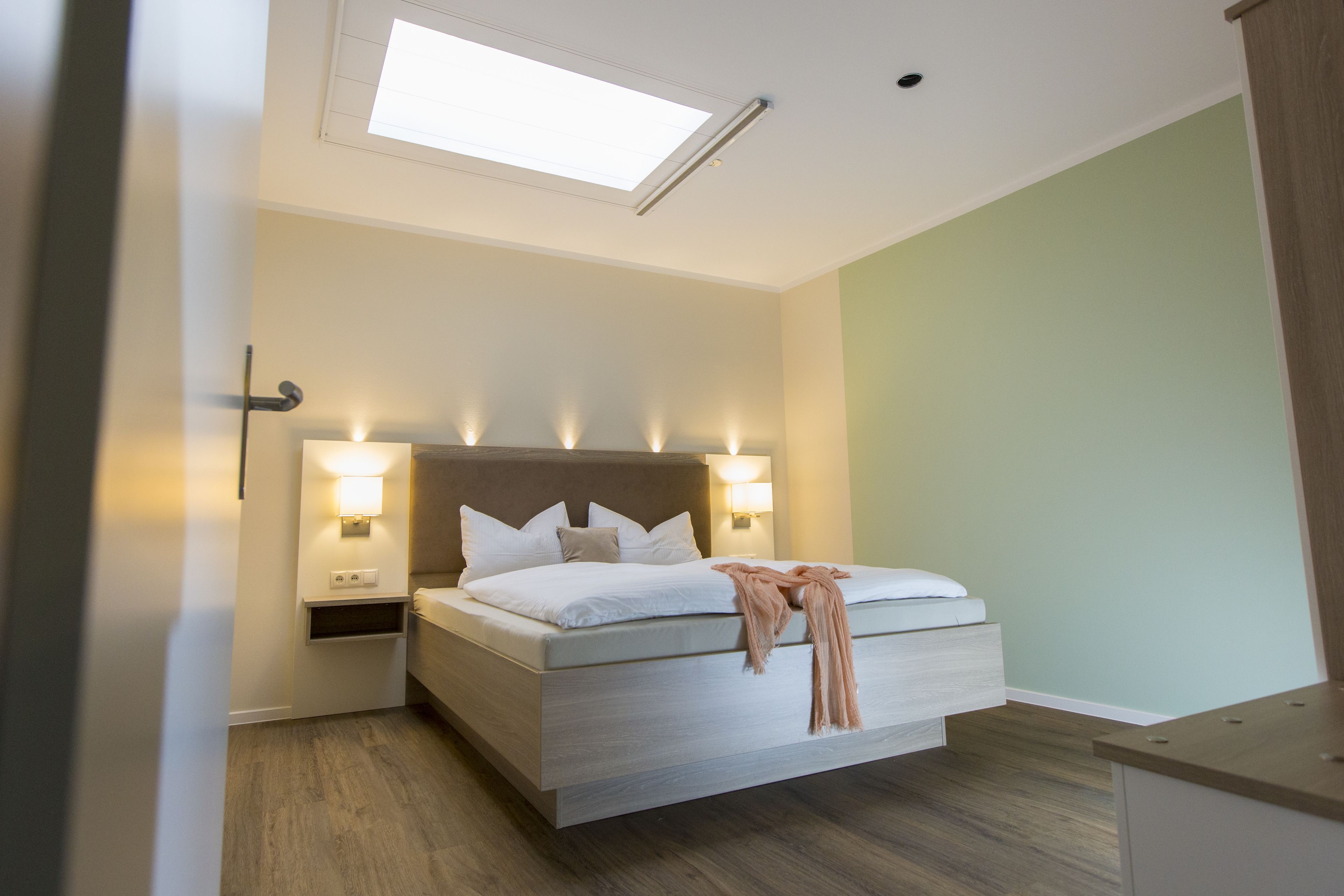 A modern bedroom with a skylight, a bed with white linens, two bedside lamps, and a wooden nightstand.