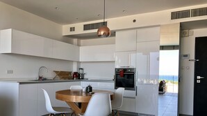 A modern kitchen with white cabinetry, a built-in oven, and a dining area with a wooden table and white chairs. - Elifelet 26 (Tel Aviv)