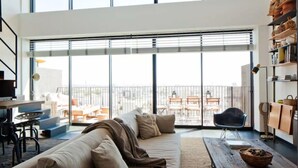 A spacious living area with a large sliding glass door leading to an outdoor patio. There is a sofa, a wooden table, and a chair. - Elifelet 26 (Tel Aviv)