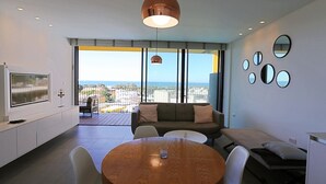 A modern living room with a wooden dining table, a sofa, and a TV on the left. - Elifelet 26 (Tel Aviv)