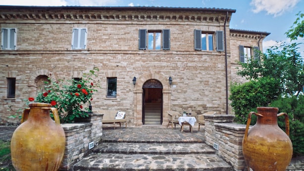 Un bâtiment en pierre avec une entrée centrale, des marches menant à cette entrée et deux grands vases de chaque côté.