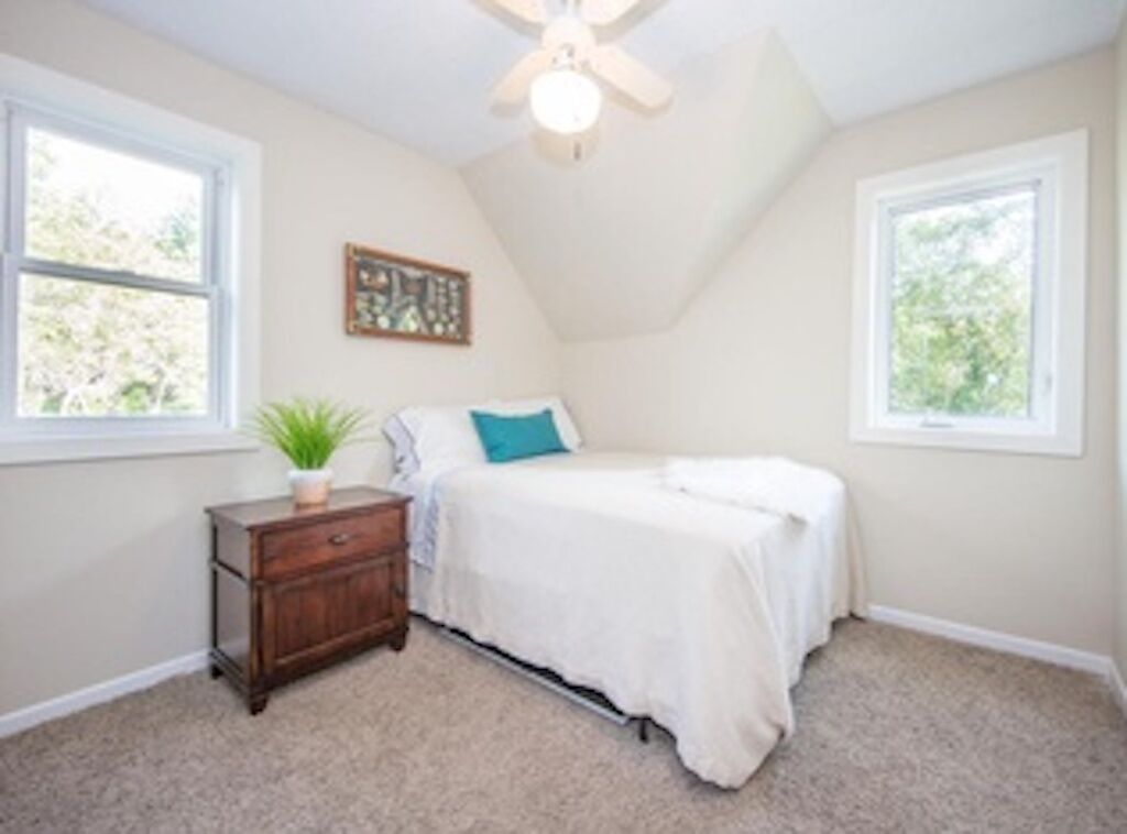 A bedroom with a bed, a nightstand, a ceiling fan, and two windows.