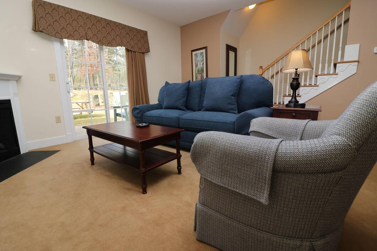 A living room with a blue sofa, a patterned armchair, a wooden coffee table, and a lamp on a side table.