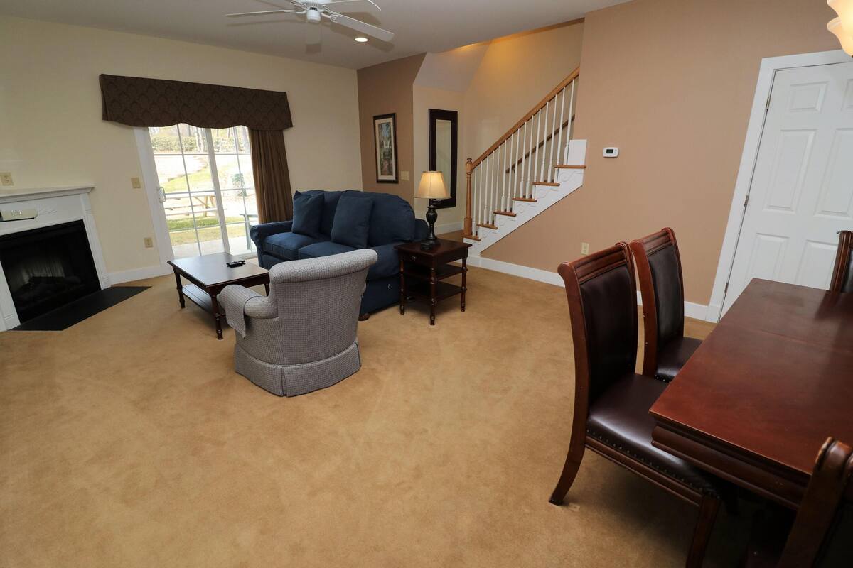 A living room with a fireplace, a sofa, a chair, a dining table, and a staircase.
