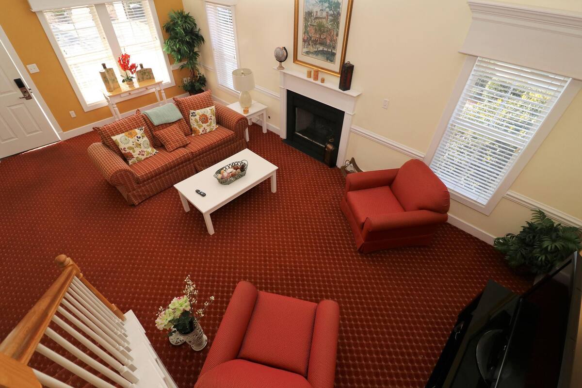 A living room with a red carpet, a fireplace, a sofa set, and a television.