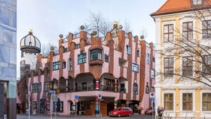 A building with a pink facade, multiple balconies, and a red car parked in front.