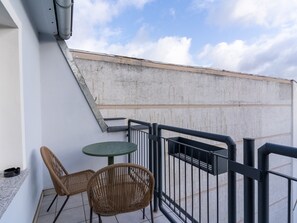 A balcony with two wicker chairs, a small round table, and a metal railing. - Limehome Magdeburg Hasselbachplatz (Magdeburg)