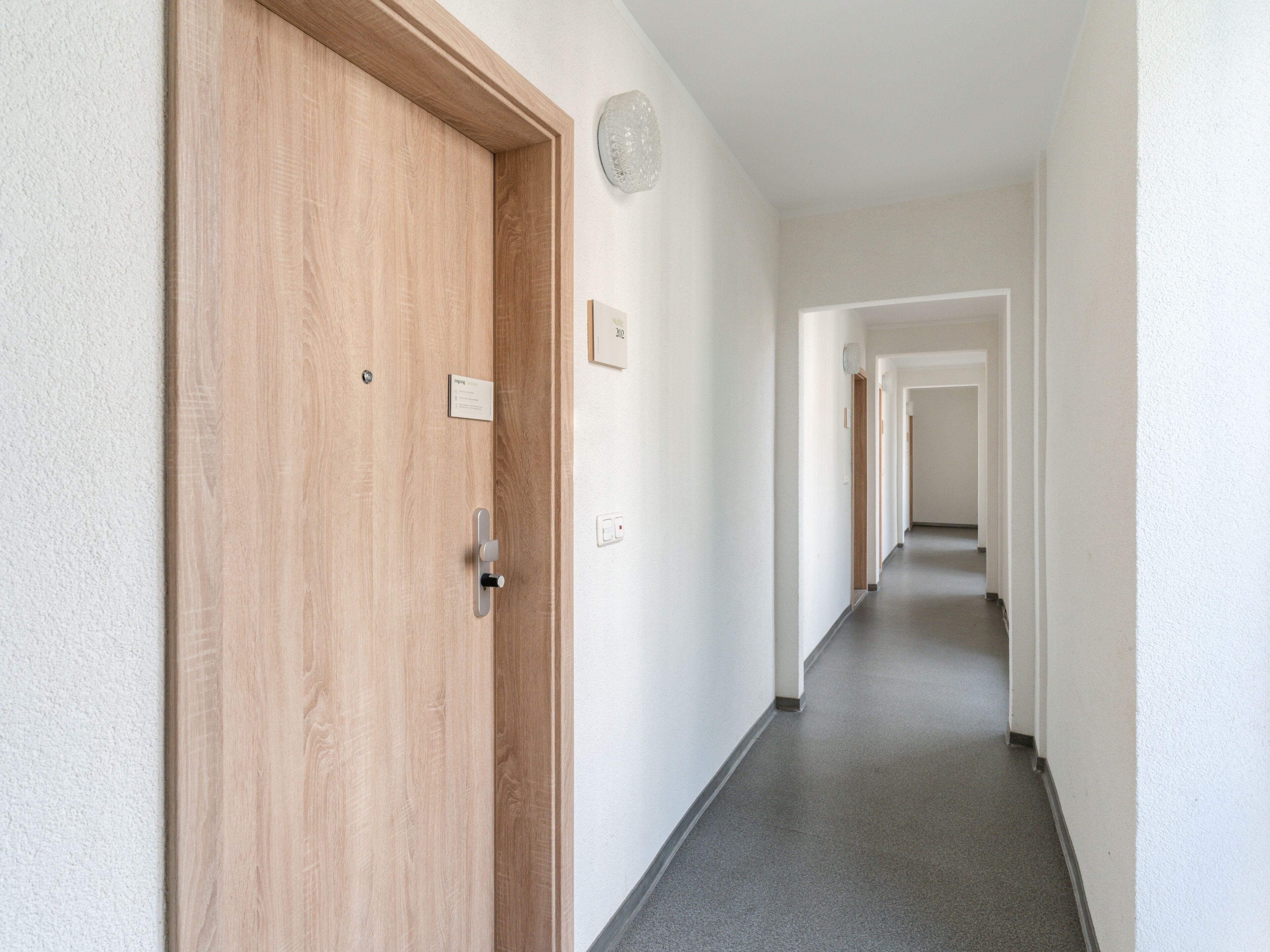 A hallway with a wooden door, a light switch, and a wall-mounted light fixture.