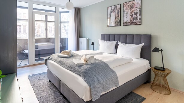 A modern bedroom with a large bed, a side table, a floor lamp, and two wall art pieces.