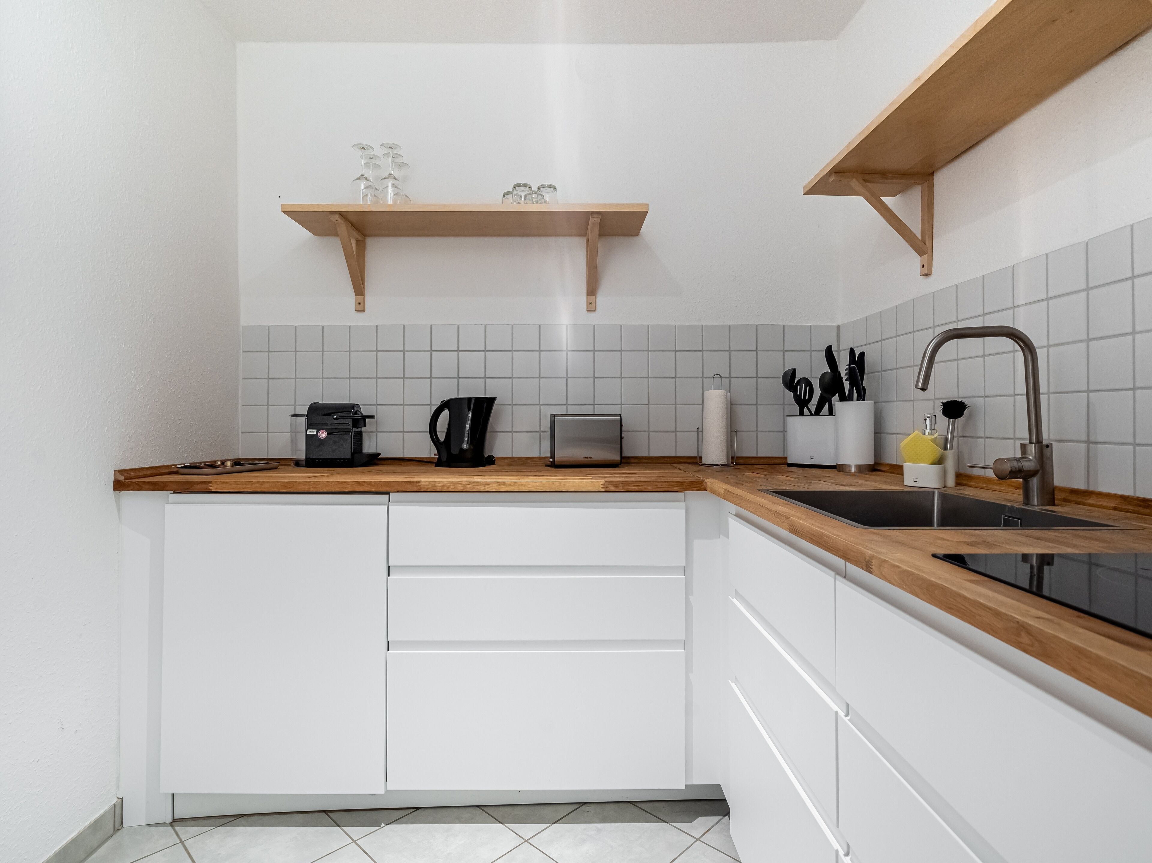 Una cocina moderna con armarios blancos, encimera de madera, cafetera, hervidor y un lavabo con grifo.