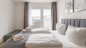 A hotel room with a bed, a window with curtains, a radiator, and a view of buildings outside.