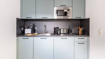 Una cocina moderna con armarios grises, un microondas de acero inoxidable, una tetera, un tostador y una cafetera.