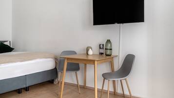 A hotel room with a bed, a wooden table with two chairs, a TV mounted on the wall, and a vase on the table.