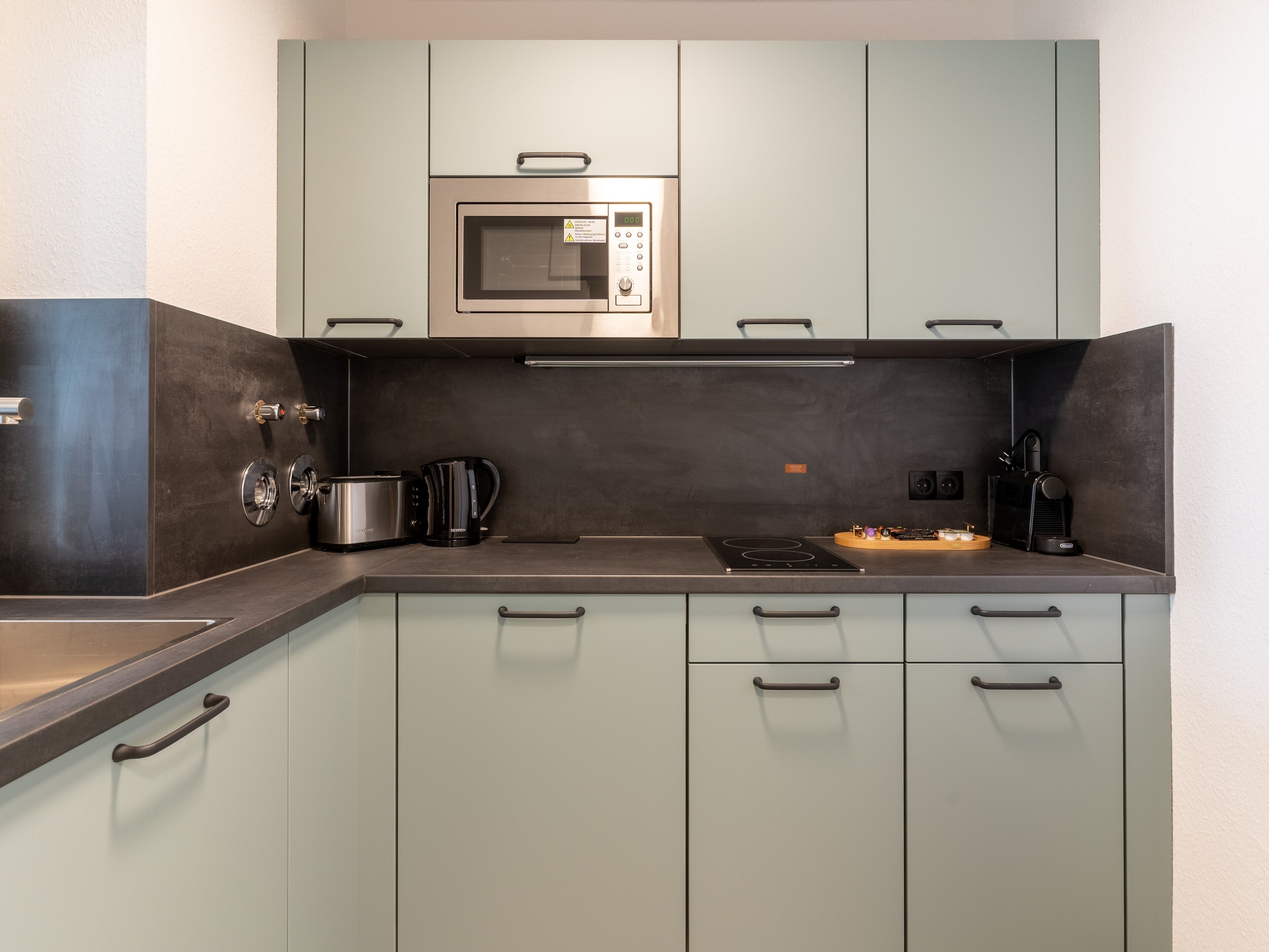 A modern kitchen with a built-in microwave, a coffee maker, and a kettle.