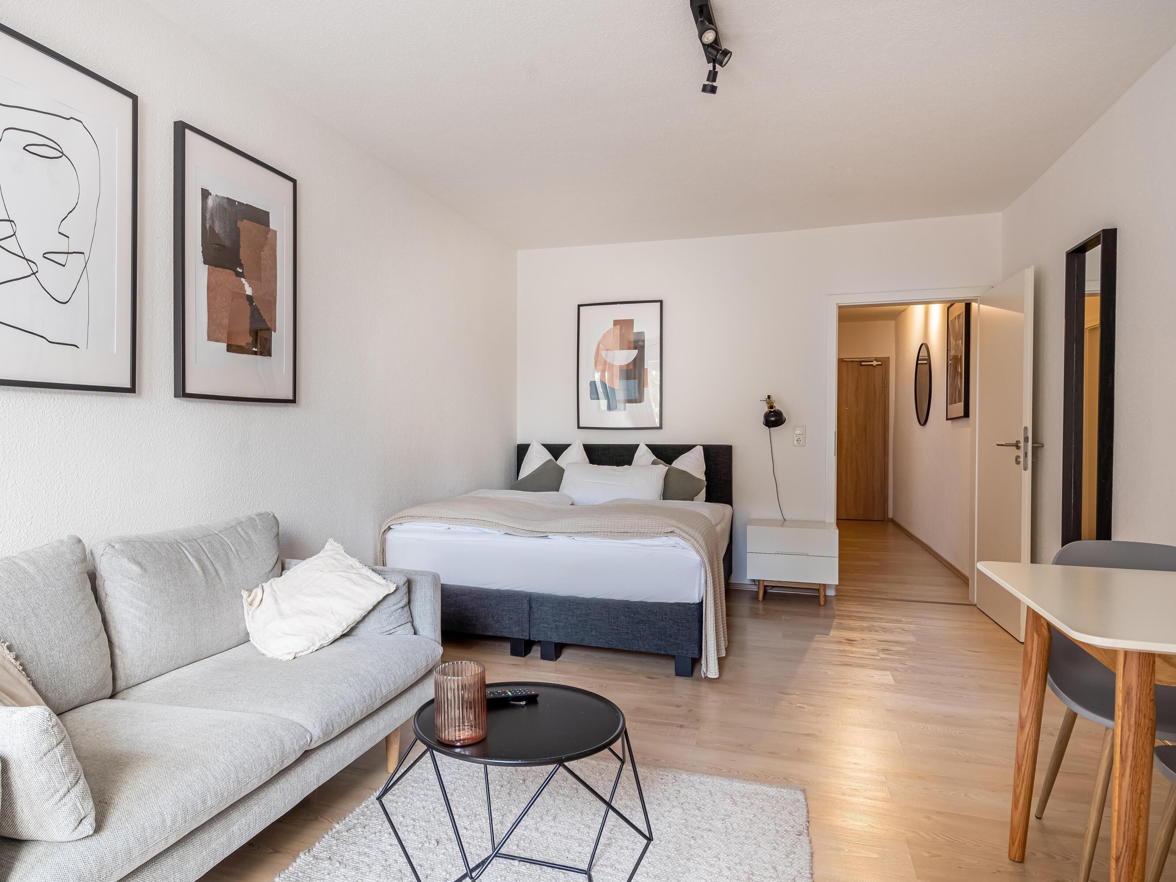 A modern bedroom with a bed, a grey sofa, a small round table, and a desk.