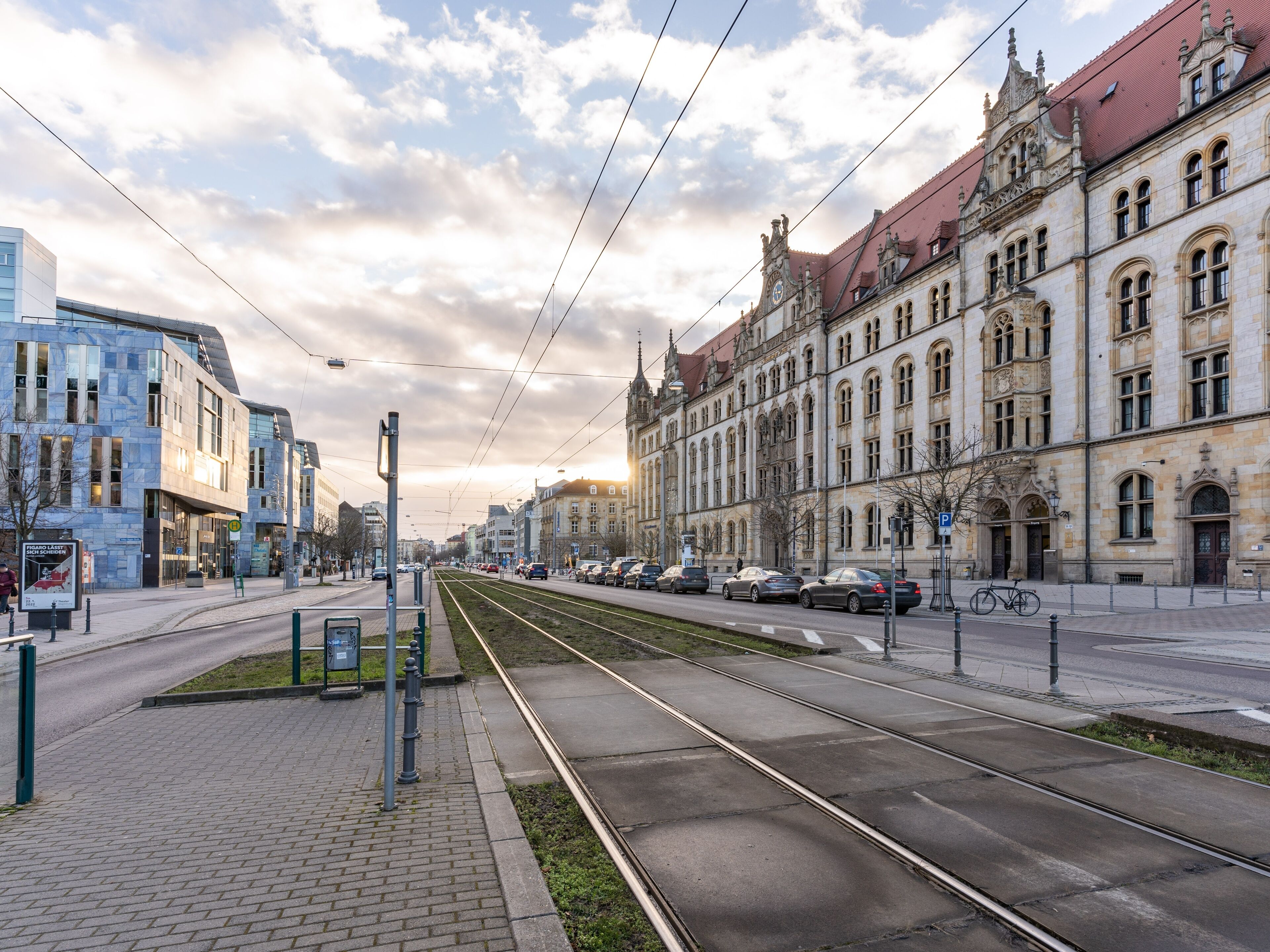 A street with tram tracks, a modern building, and a historic building with ornate architecture.