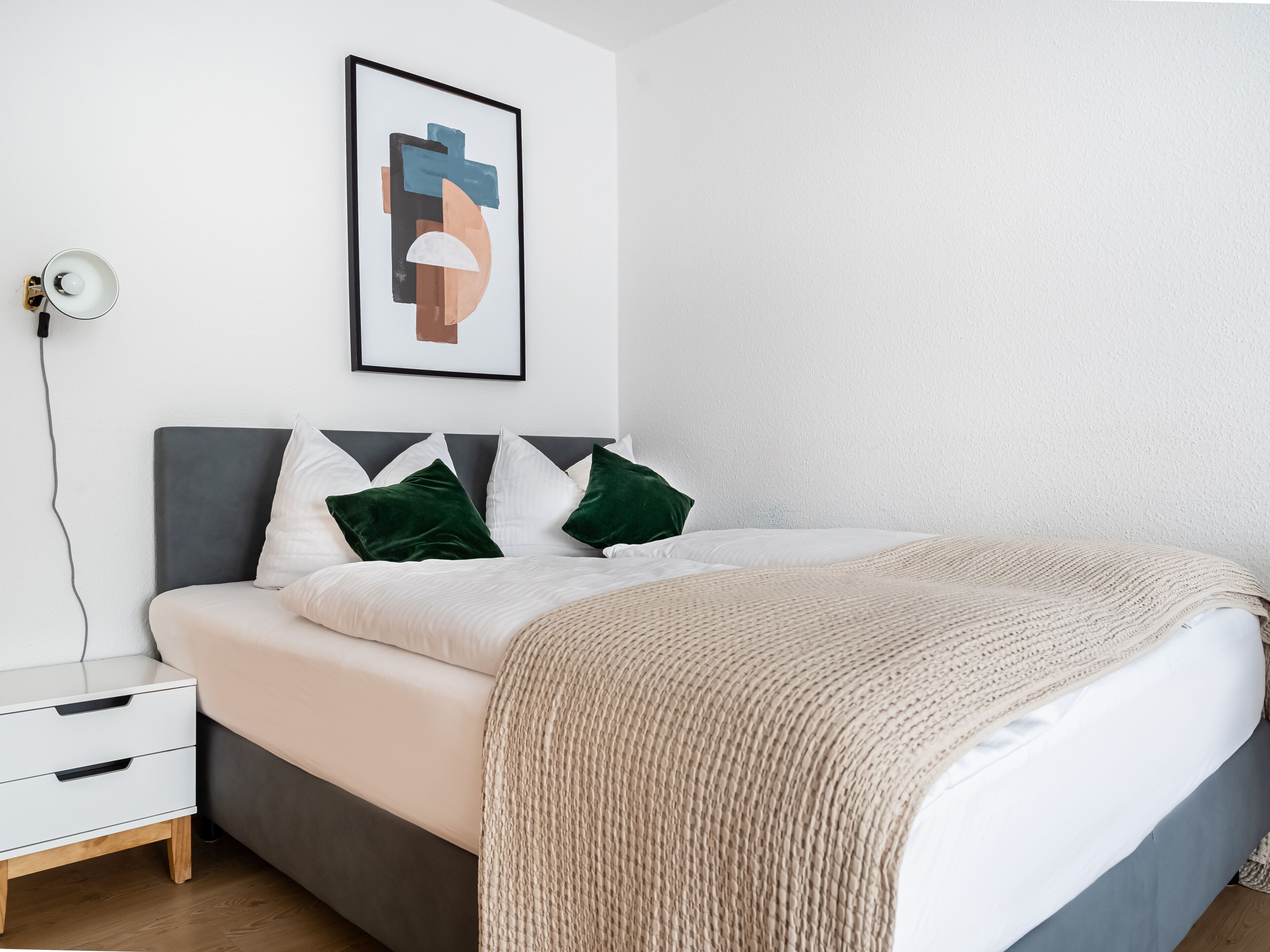 A neatly arranged bedroom with a bed, bedside table, and a wall-mounted lamp.